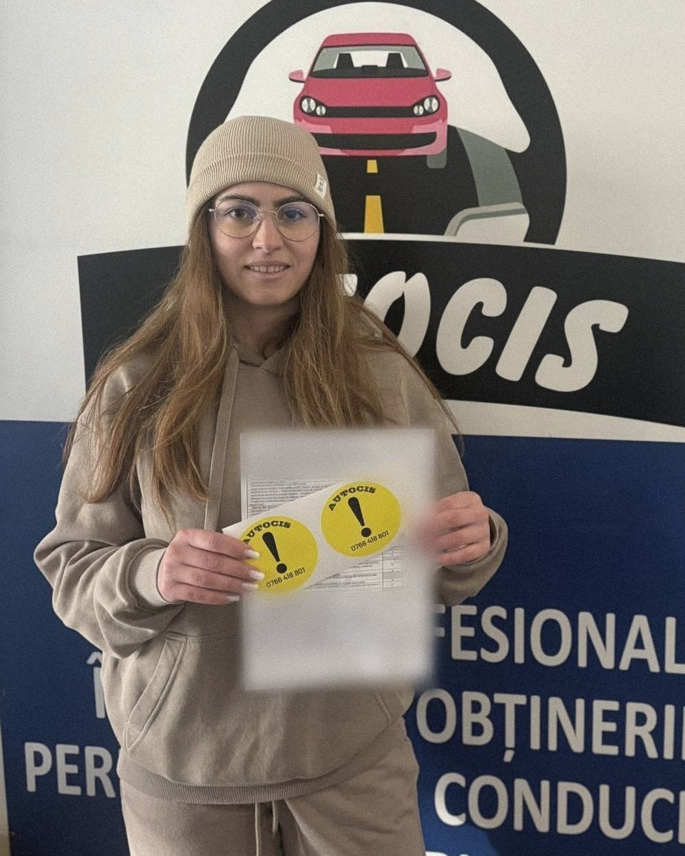 Absolventă a Școlii de șoferi Autocis cu actele de la examen și semnele de începător, în fața bannerului Școlii de șoferi Autocis