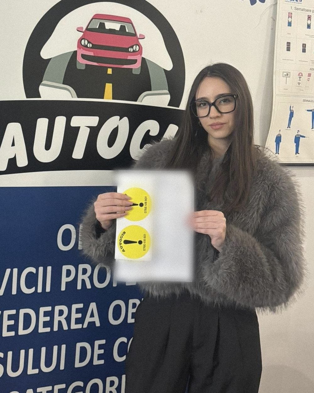 Absolventă a Școlii de șoferi Autocis cu actele de la examen și cele două semne de începător, lângă sigla școlii din sediu