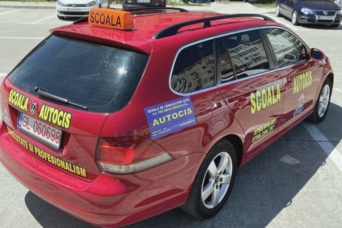 Volkswagen Golf Variant roșu al școlii, cu cutia „ȘCOALA” pe plafon, în parcarea unui bloc din Tecuci